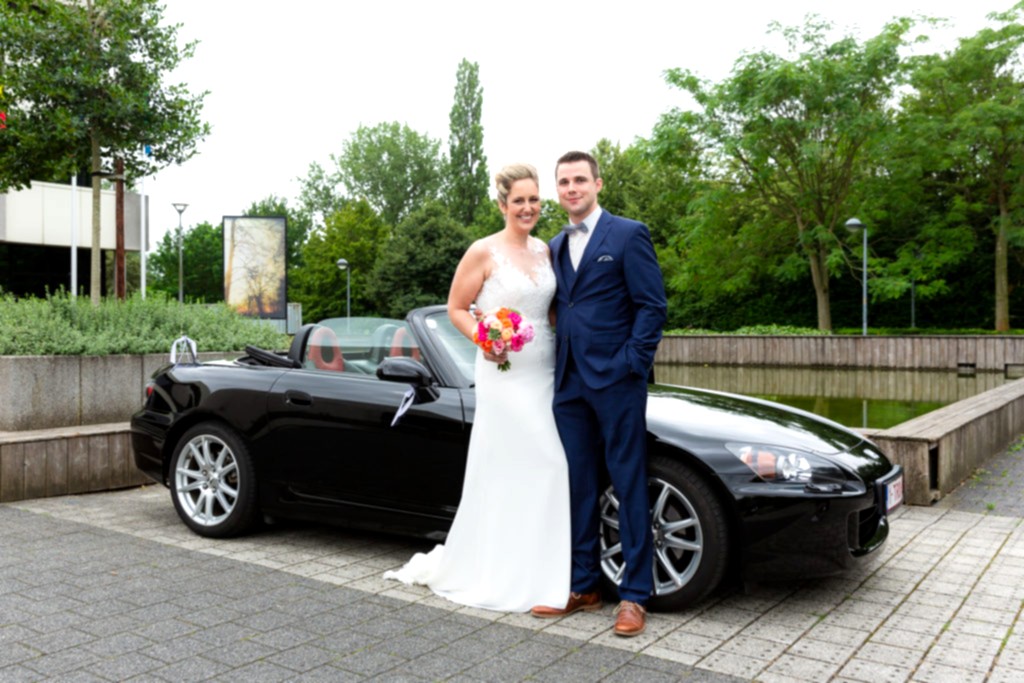 bride and groom standing in front of sports car