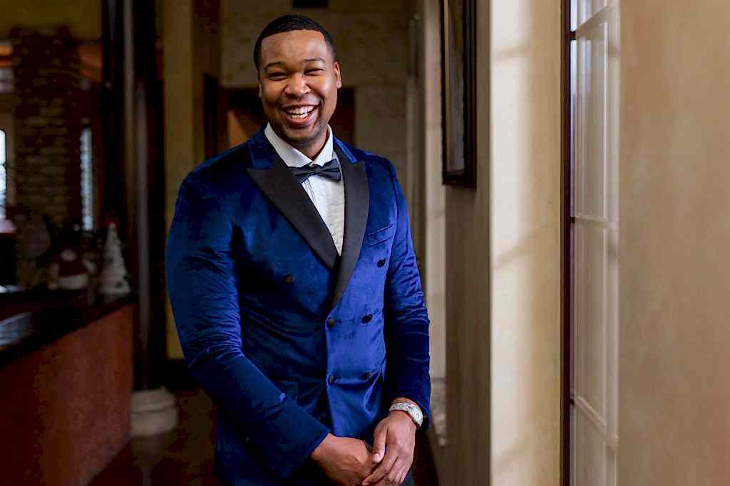 Groom smiling while in his wedding suit standing in front of a window at Stoney ridge villa