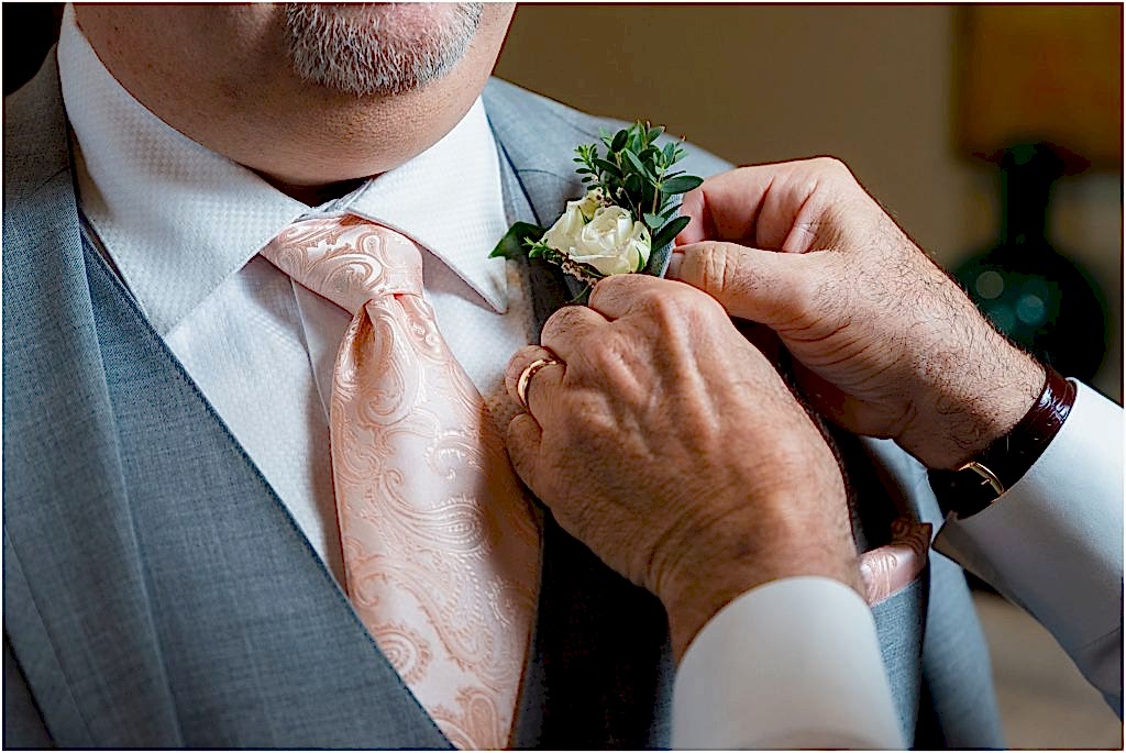 Dallas wedding photographers zoom in on groom's small boutonniere with white roses and greenery