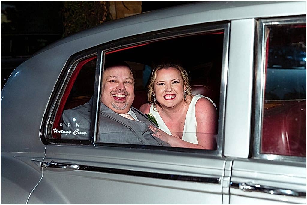 Dallas wedding photographers capture bride and groom grinning through an open window in the back of a vintage silver car