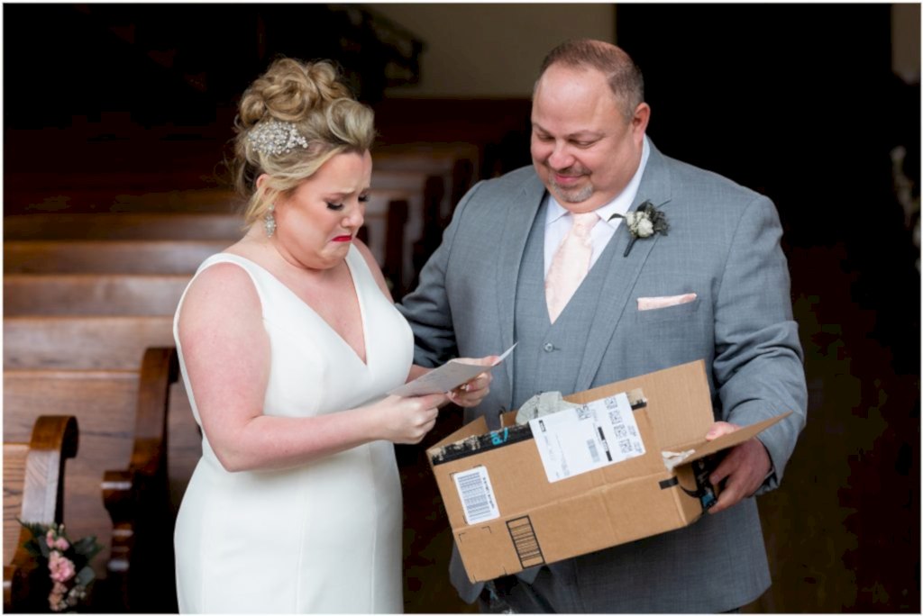 The groom holds and open package while the bride gets emotional reading a card at their luxury wedding venue by Dallas wedding photographer