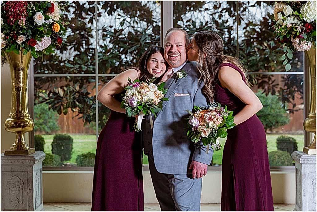 Groom gets kissed and hugged by daughters on either side posing for Dallas wedding photographers