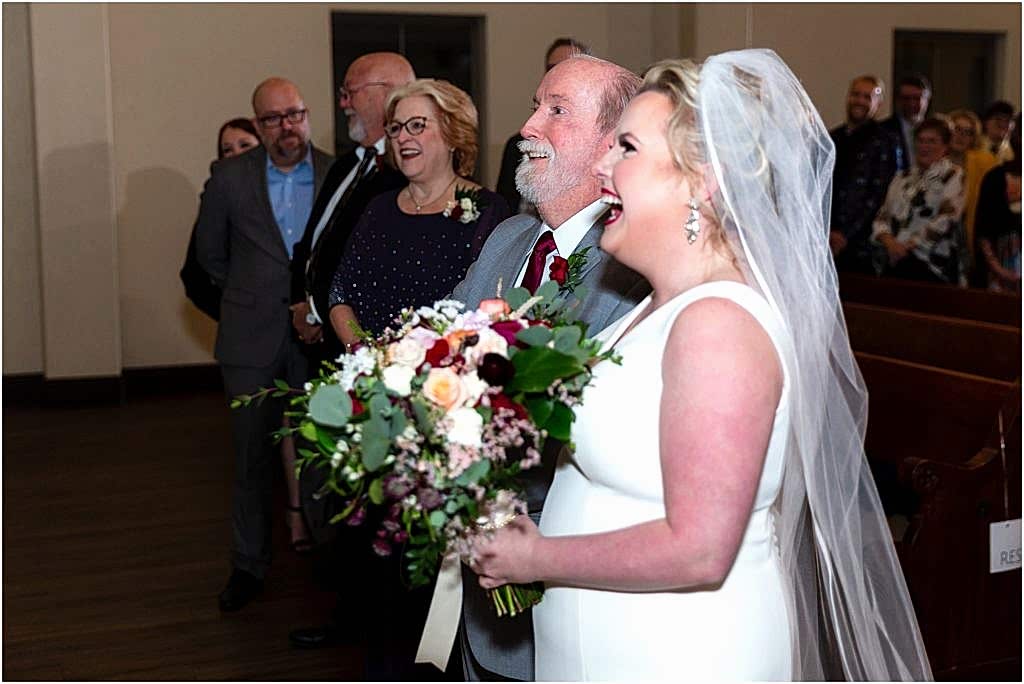 The bride and her father smile as the father gives her away at the altar captured by Dallas wedding photographers