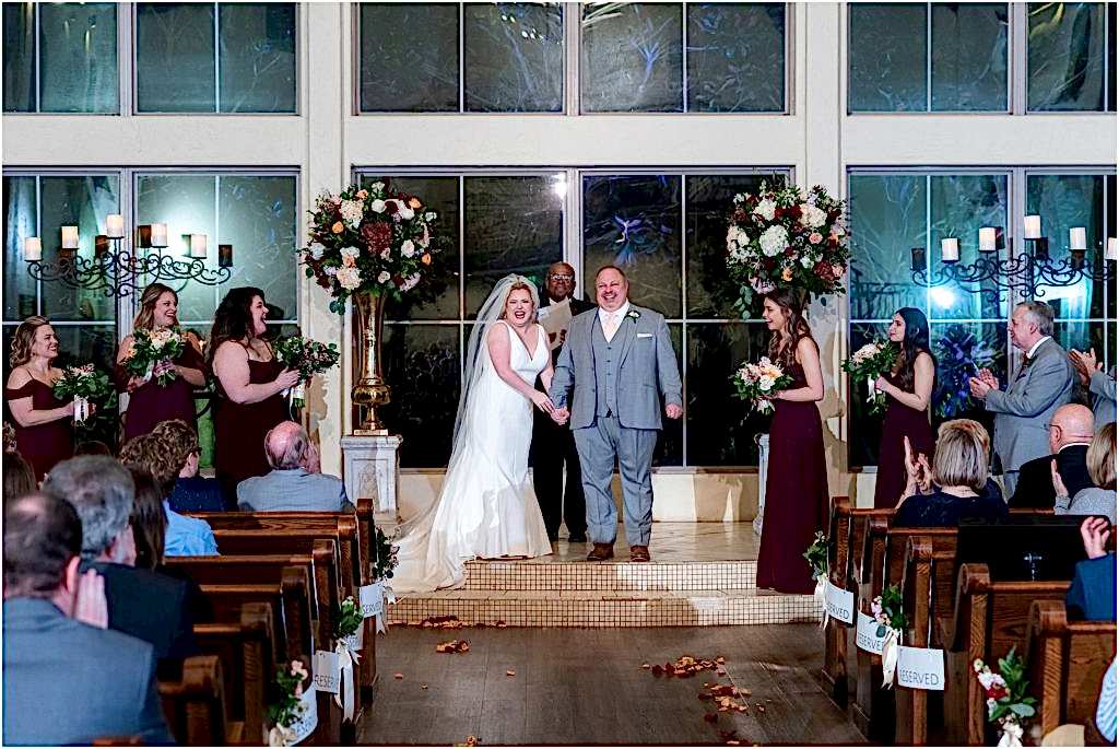 Bride holds groom's hand and smiles in front of officiant in chapel of luxury wedding venue captured by Dallas wedding photographers