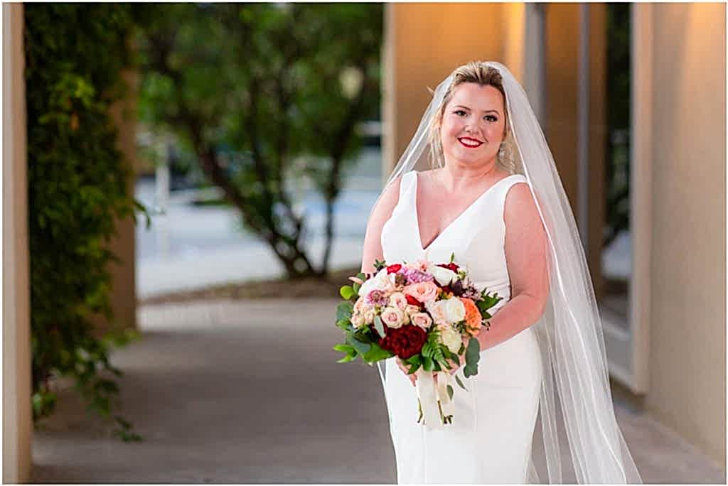 The bride stands slightly off center of the photo with her bouquet covering her hands at a Dallas wedding venue captured by Dallas wedding photographers