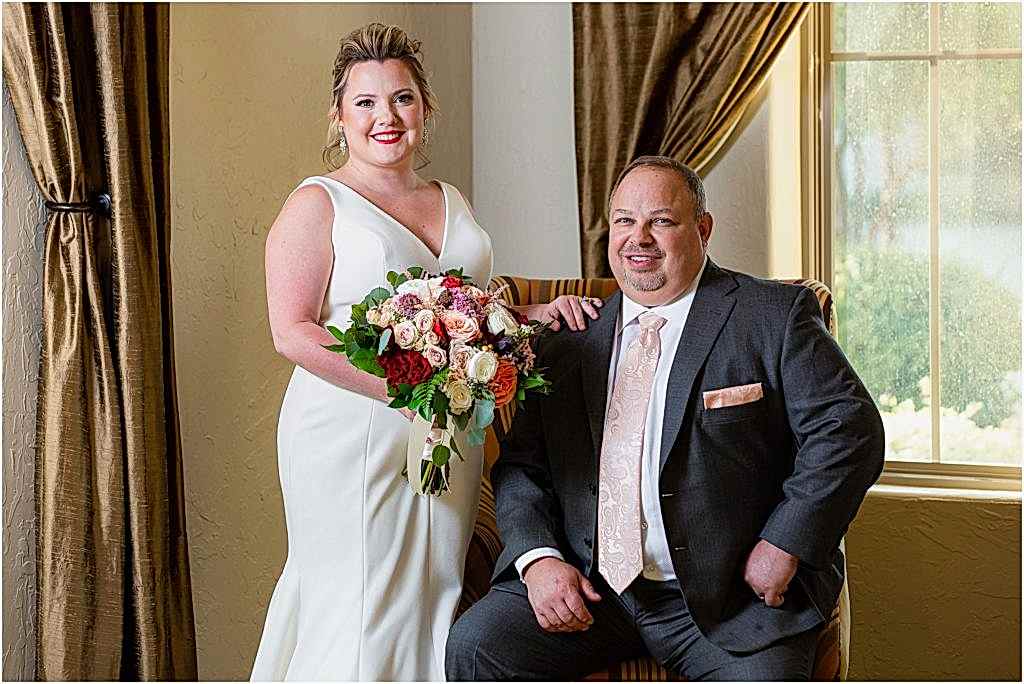 Bride puts her hand on groom's shoulder as he is seated next to gold curtains in Dallas wedding venue photographed by Dallas wedding photographers