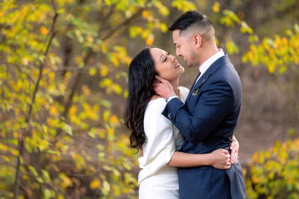 Couple smiling at each other with yellow foliage behind them during Arbor Hills Nature Preserve engagement session