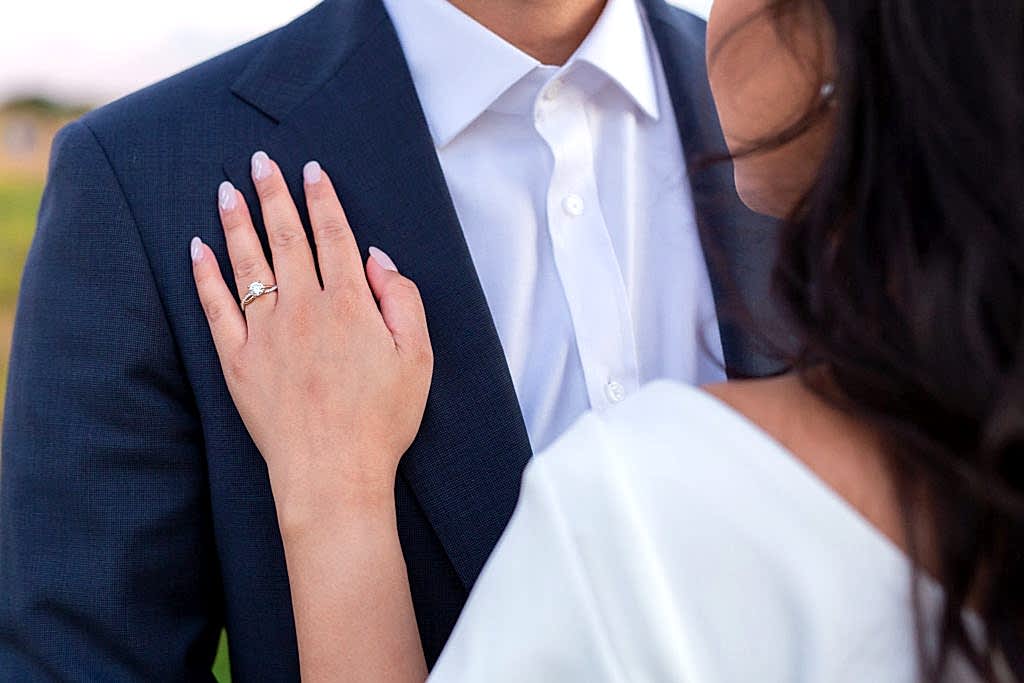 Detail shot of engagement ring as the woman holds her hand over the grooms suit coat