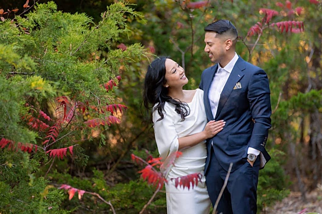 Arbor Hills Nature Preserve Engagement Photography of couple smiling at each other surrounded by green and red foliage