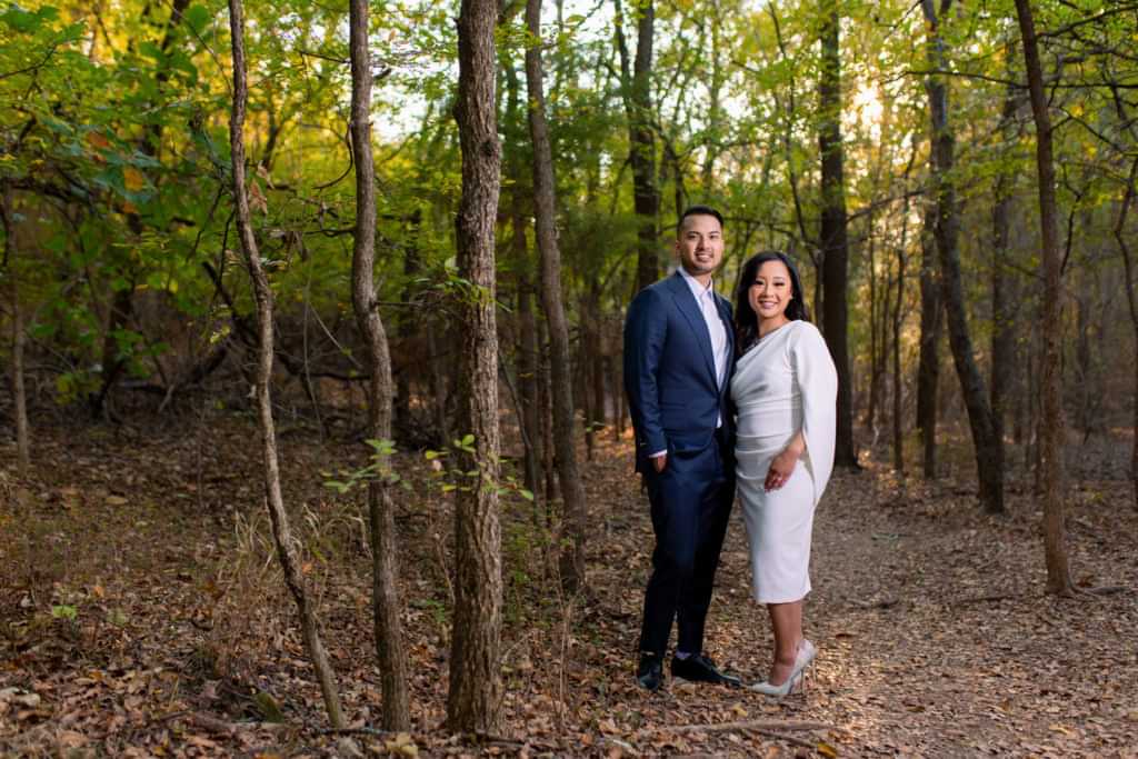 A Plano park engagement session at Arbor Hills Nature Preserve with bride and groom smiling at camera surrounded by wooded trees