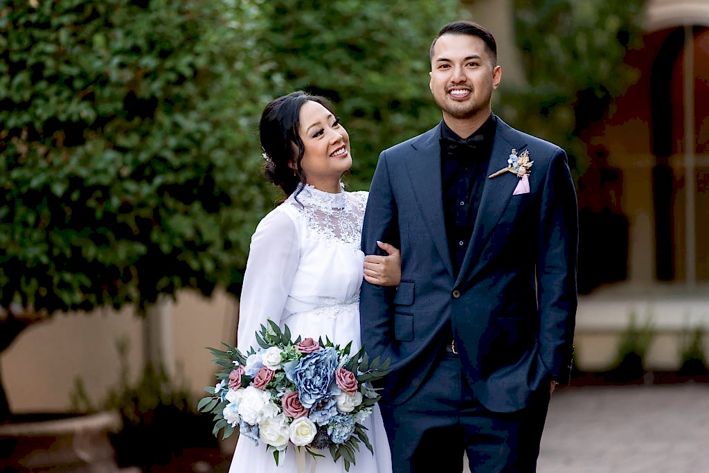 bride holding her grooms arm and smiling up at him while he holds his hands in his pockets for their outdoor wedding portraits