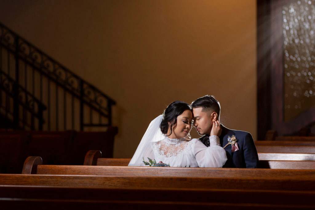 Bride and groom snuggled up in pew in the Chapel at Ana Villa's ceremony chapel in Texas