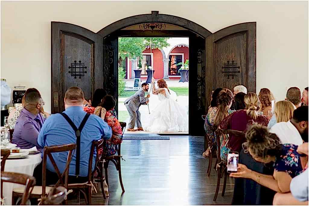 bride and groom entering their wedding reception by ringing a large bell outside the doors while guests watch