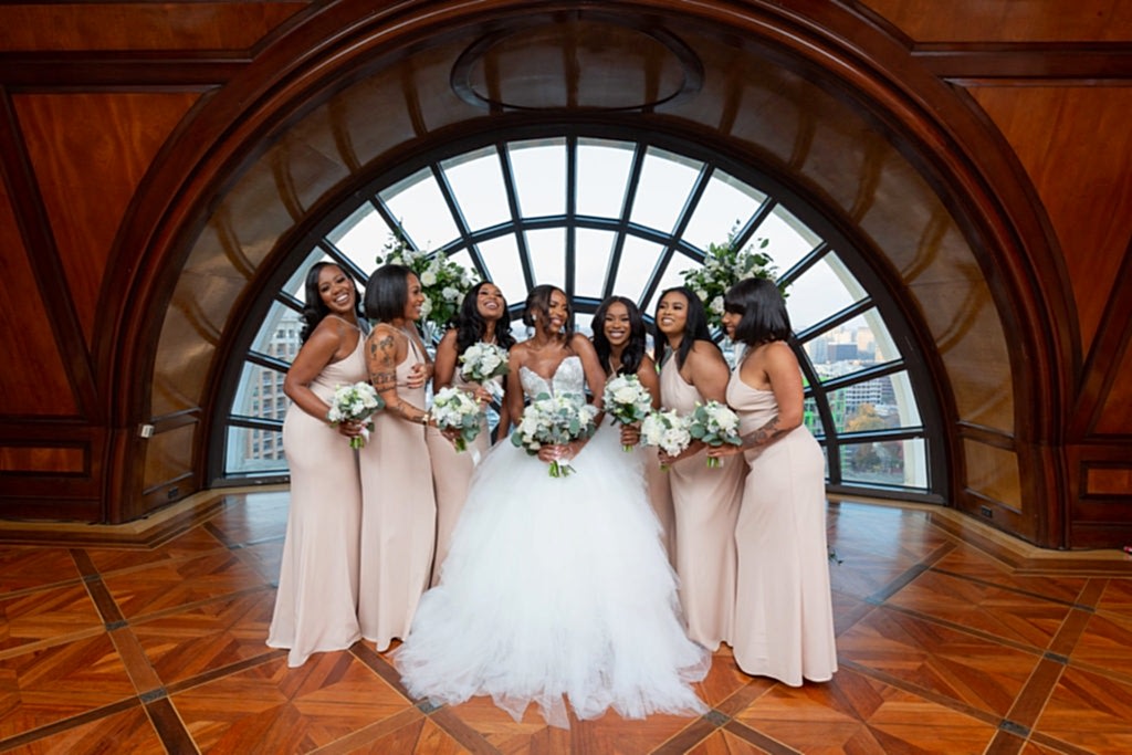 bride with her bridesmaids who are wearing light pink bridesmaids dresses and holding white rose bouquets