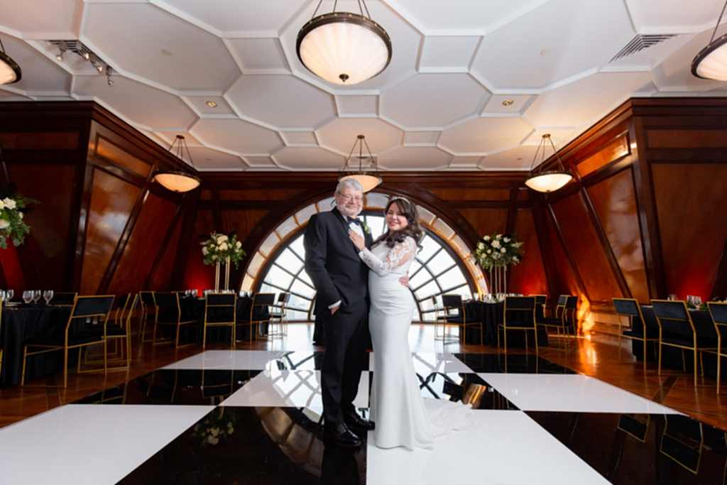 wedding portrait with bride and groom embracing in their reception space with a large window in the distance at the Hotel Crescent Court