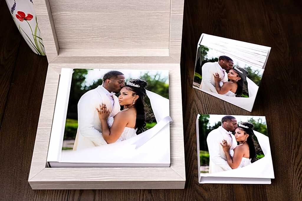 an heirloom wedding album with white spine and an acrylic photo cover of groom kissing bride on the temple during wedding at knotting hill place venue sitting inside of a luxury wooden box accompanied by two smaller duplicate parent albums with the same image