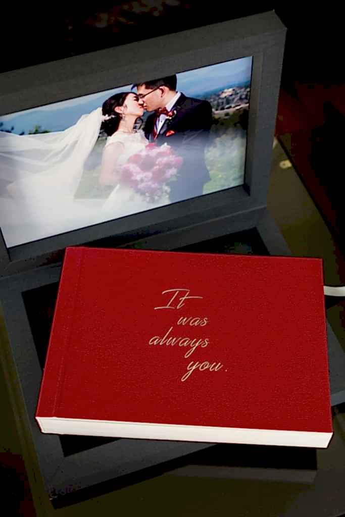 custom red leather heirloom wedding album sitting inside blue linen box with image of bride and groom kissing inside front lid