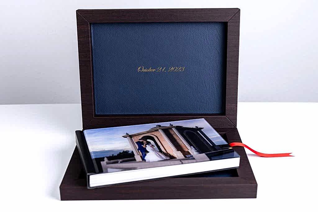 an heirloom wedding album with black spine and an acrylic photo cover of bride and groom hugging on stoney ridge villa wedding venue's rooftop sitting inside of an open luxury dark wood and blue leather box
