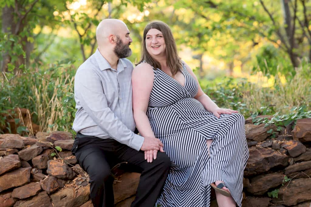 Engaged couple sitting on rocks in heavily wooded area laughing at each other on Texas Women's University in Texas during engagement session