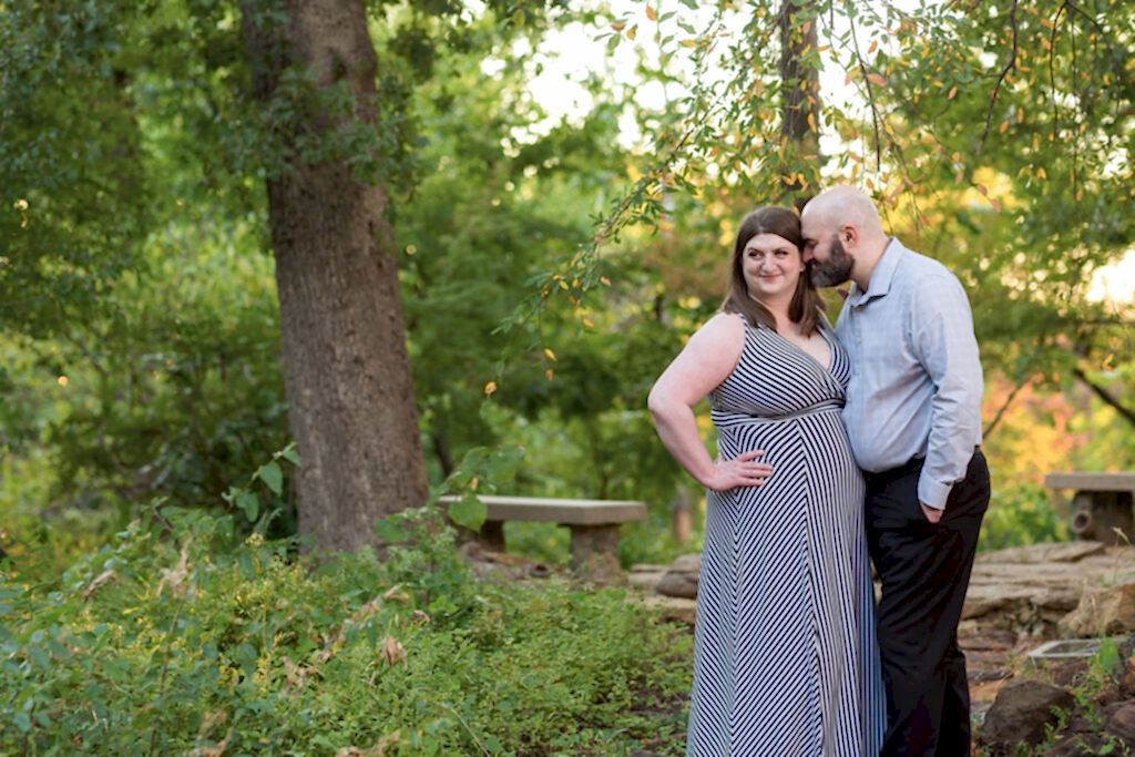 Man nuzzling into his fiancée in a forest with rock pathway and lush trees behind them during engagement session at TWU