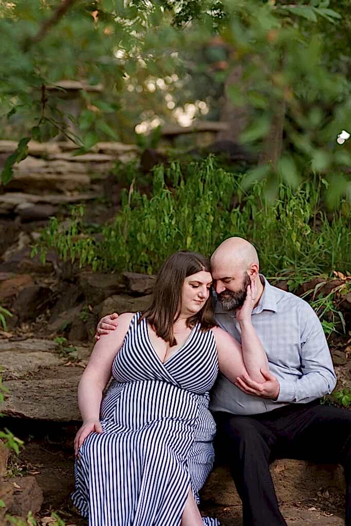 Engaged couple sitting forehead to forehead on a rock stair pathway with foliage surrounding them