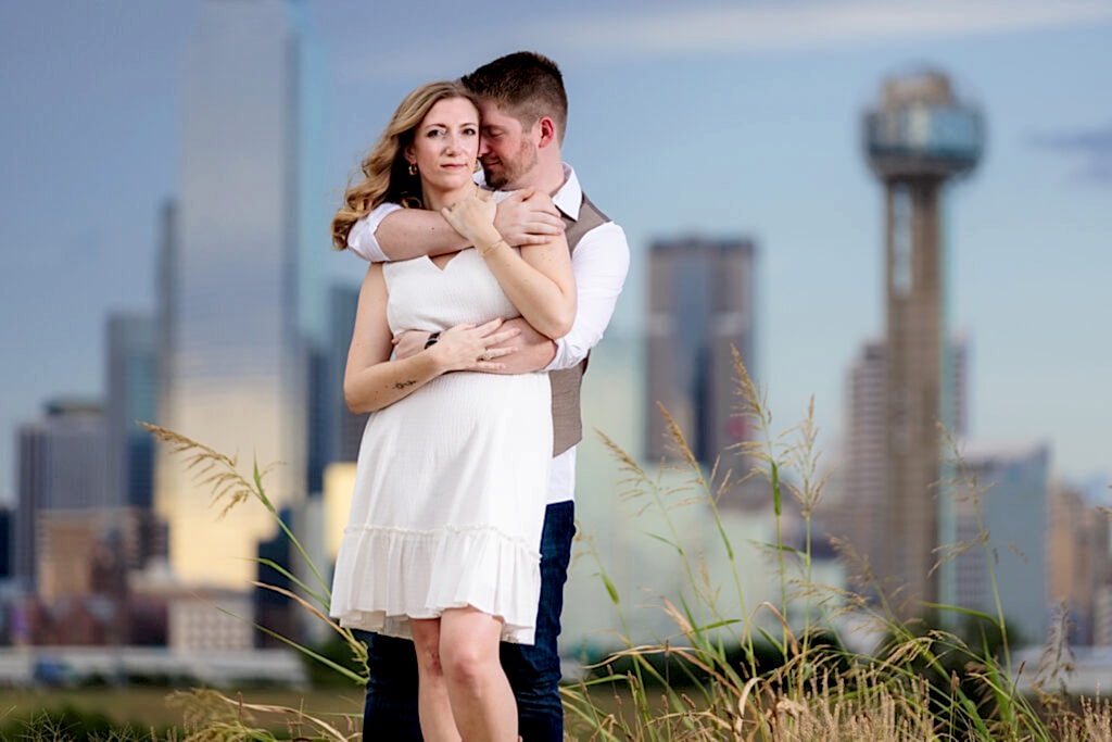 Dallas wedding photographers captures man nuzzling into his fiancee's neck during outdoor engagement session wearing white dress