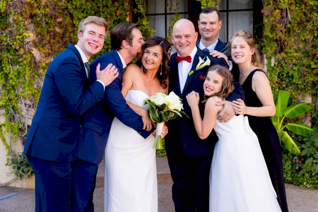 Wedding couple standing together surrounded by family hugging in on and kissing them at stoney ridge villa wedding venue