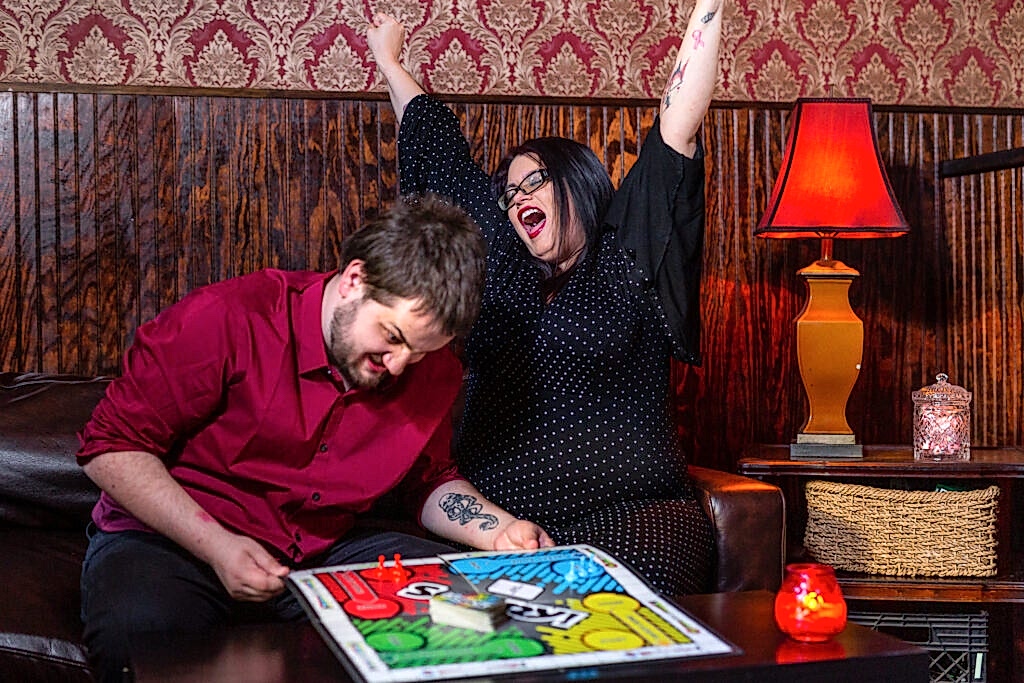 Bride cheering and groom angry playing Sorry board game during engagement session in Deep Ellum Texas