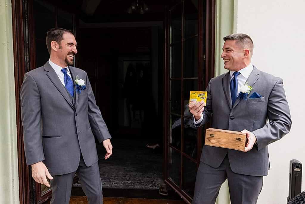 Groom gifting groomsmen a box of crayons and them both laughing