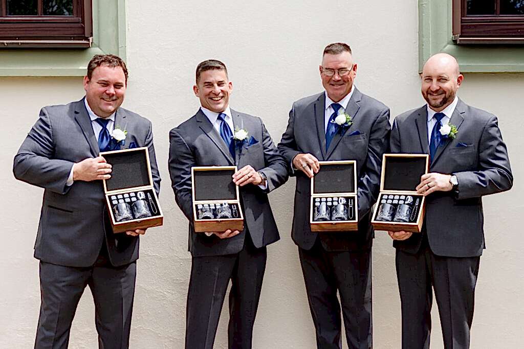 Groomsmen opening gift boxes of whiskey glasses