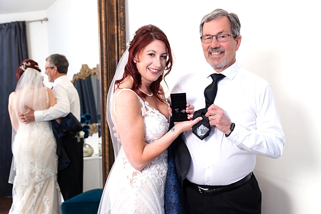 Bride and dad holding tie and cufflinks smiling