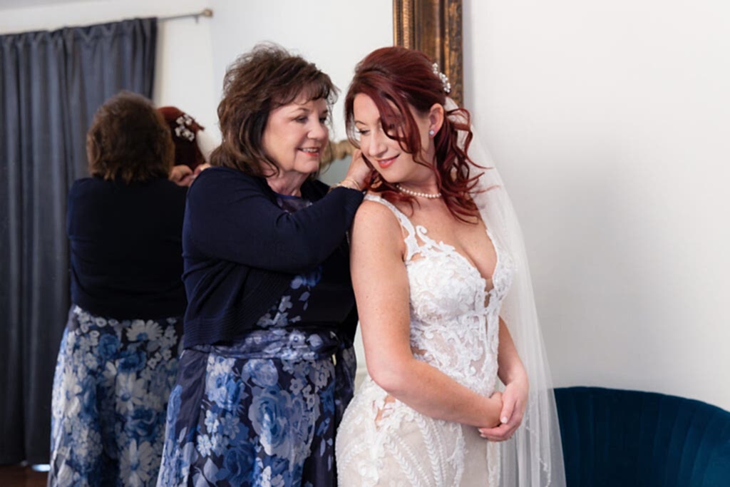 Mom putting pearl necklace on bride in front of large mirror in Stoney Ridge Villa bridal suite
