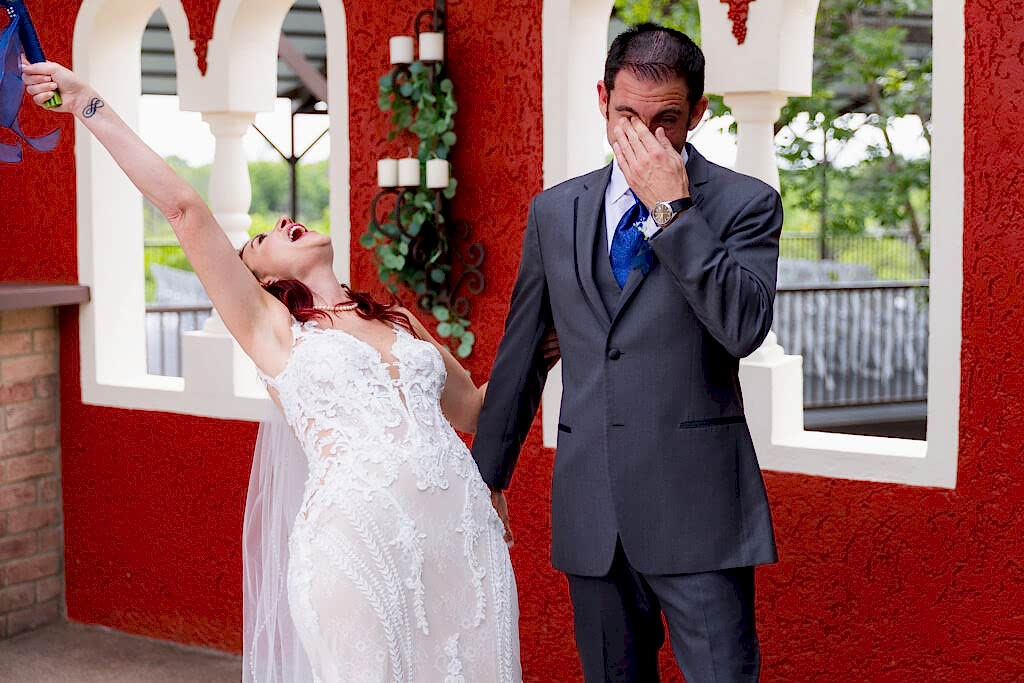 Bride celebrating and throwing bouquet in air while groom wipes tears