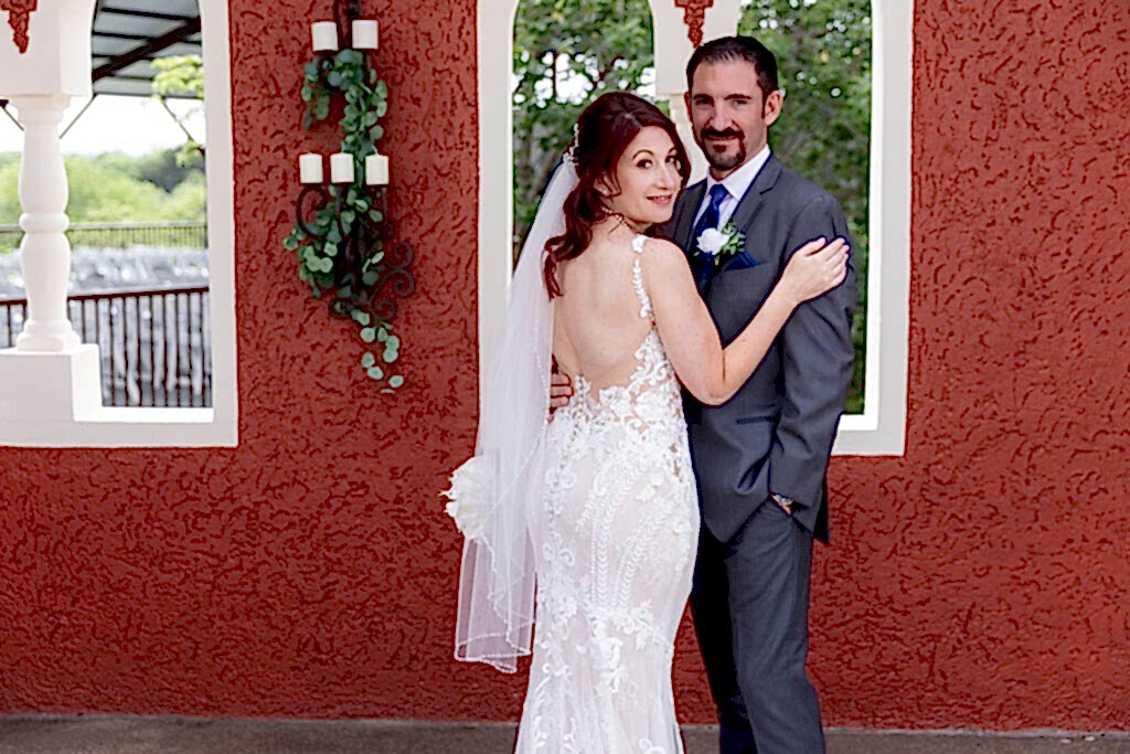 Bride looking back at camera while hugging groom in front of orange wedding venue wall