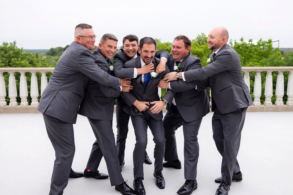 Groomsmen in grey suits jumping on groom laughing