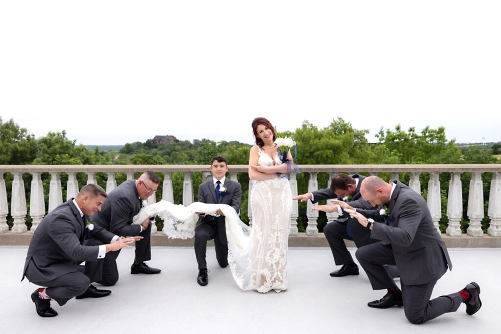 Bride with groomsmen in grey suits and blue ties bowing down to standing laughing bride