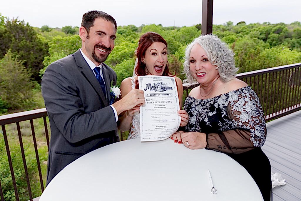 Bride and groom excitedly holding up marriage license with officiant
