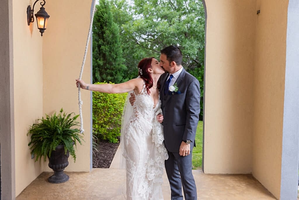 Bride and groom holding rope to bell tower while kissing at Azle TX wedding venue Stoney Ridge Villa