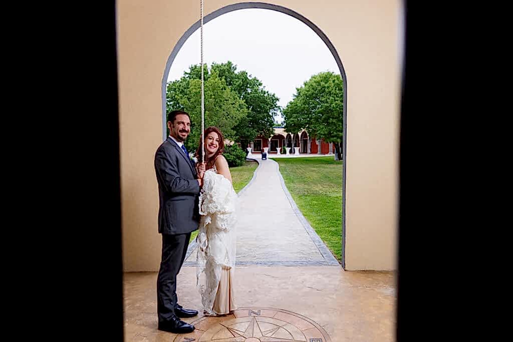 Bride and groom holding rope to bell tower smiling with Stoney Ridge Venue courtyard in the background