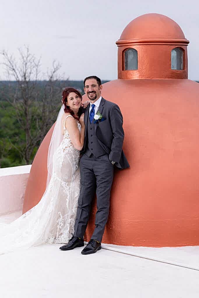 Red-haired bride and groom smiling at camera on rooftop