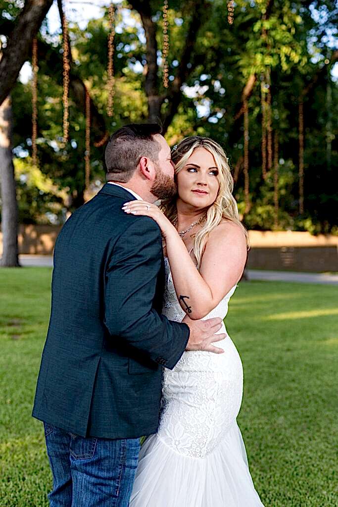 Groom kissing bride on temple under trees and hanging string lights