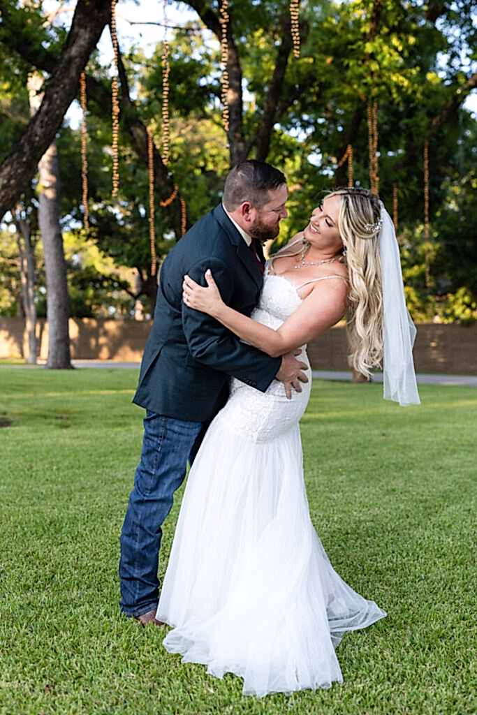 Groom dipping bride under trees and hanging string lights