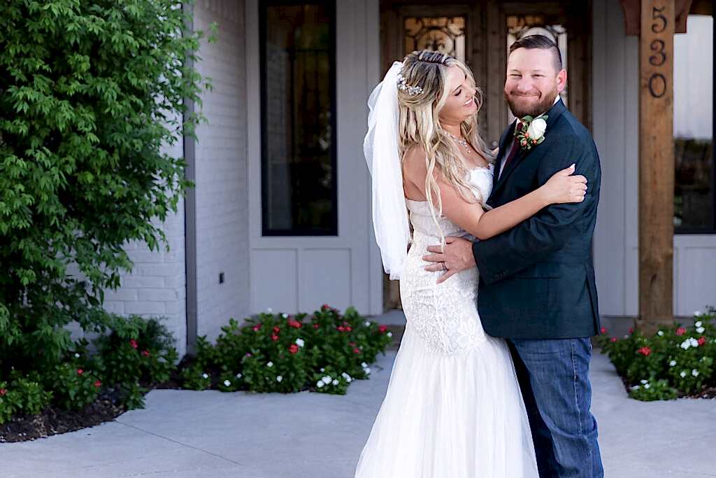 Bride looking at groom while he smiles at camera in front of hotel entrance