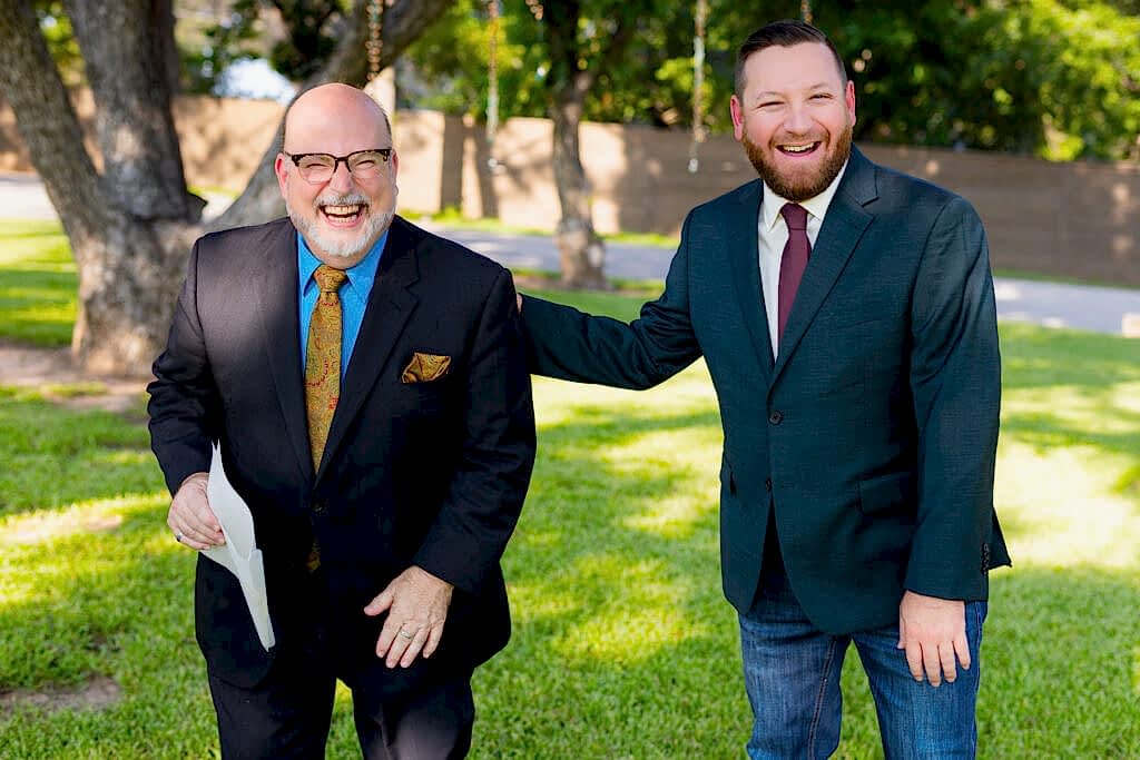 Groom laughing with officiant on lawn before wedding ceremony
