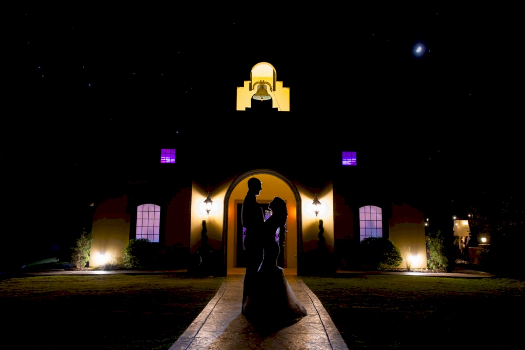 Silhouette photo of bride and groom in front of Stoney Ridge Villa's reception hall with bell tower at night with stars in the sky during Fort Worth Estate Wedding