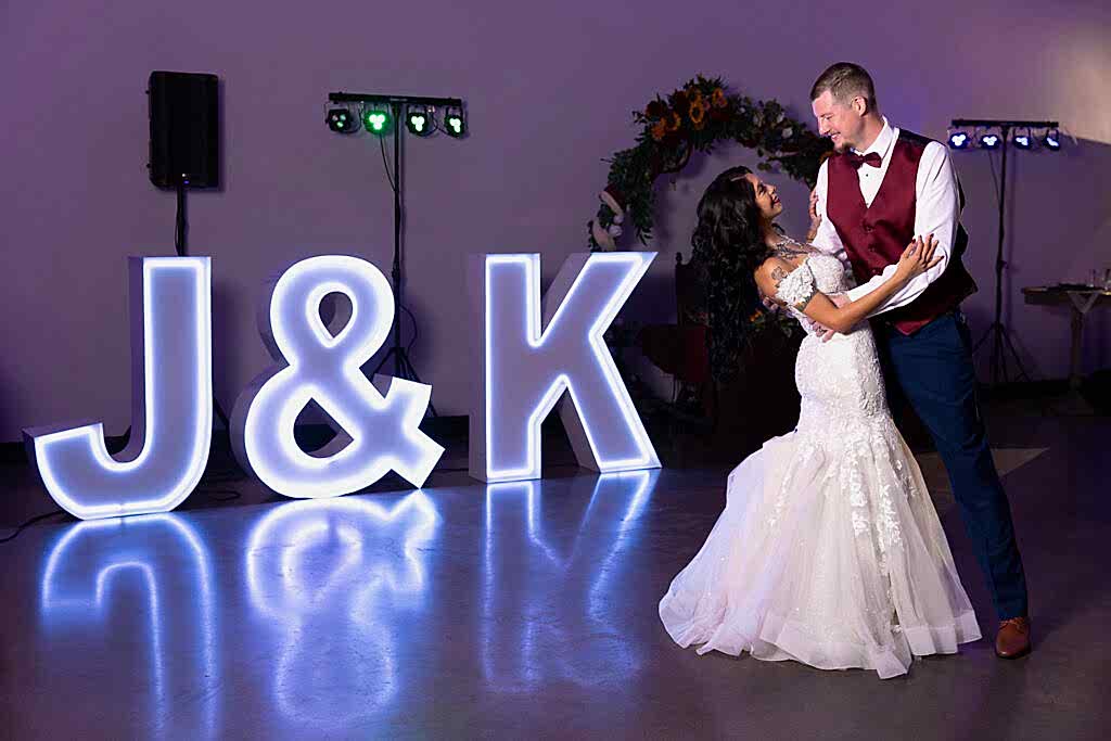 Groom in red vest dipping bride during wedding reception in front of J & K purple marquee letters