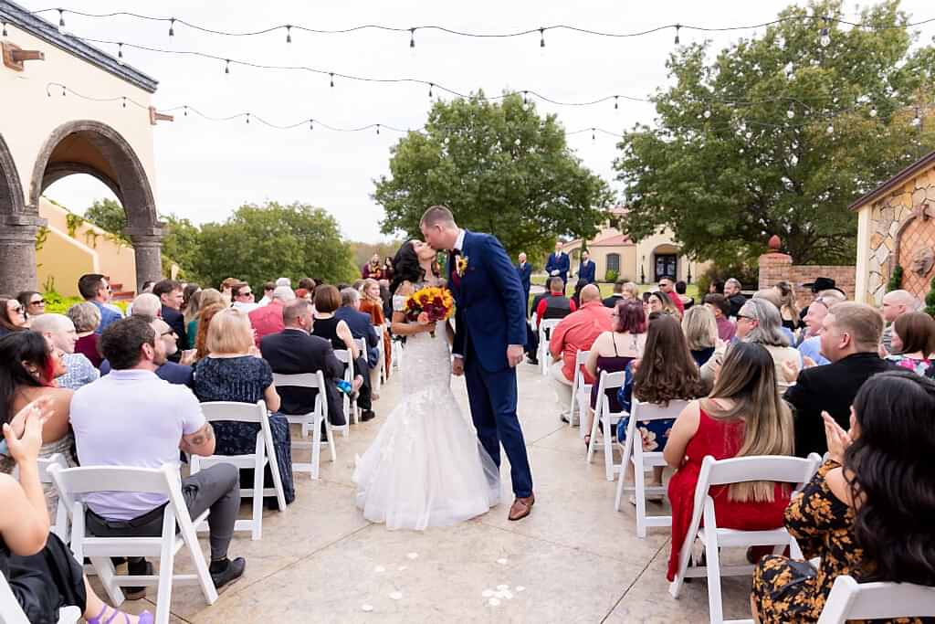 Bride and groom holding hands and kissing while walking back down the aisle after ceremony during Fort Worth Estate Wedding at Stoney Ridge Villa
