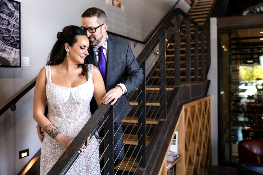 bride in a Galia Lahav Oriana sparkling a-line wedding dress standing on staircase at Prosper Wine House with groom in dark grey ted baker suit smiling into each other