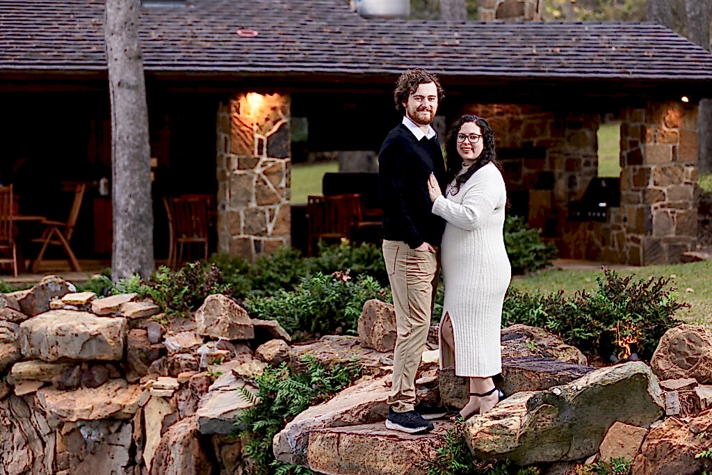 Engaged couple standing together and smiling on rocks in backyard of lakehouse