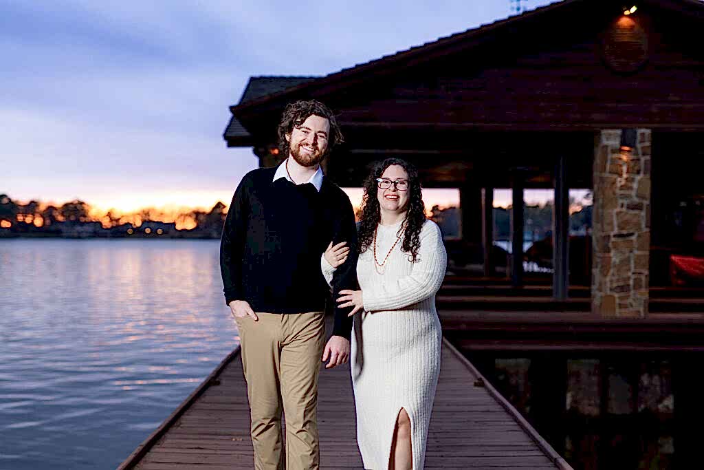 Engaged couple strolling arm in arm along their boat dock and smiling at sunset